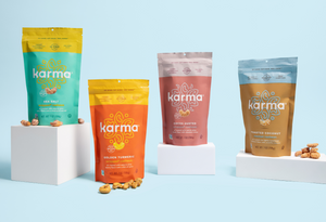 image of four 7 oz karma nuts cashews bags (coconut, cocoa, sea salt and turmeric) on light blue background 